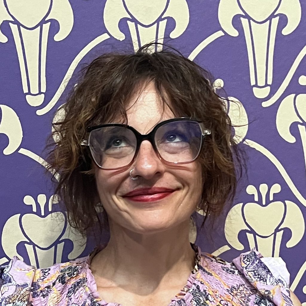 Headshot of Orit Halpern, standing in front of a purple wallpaper.