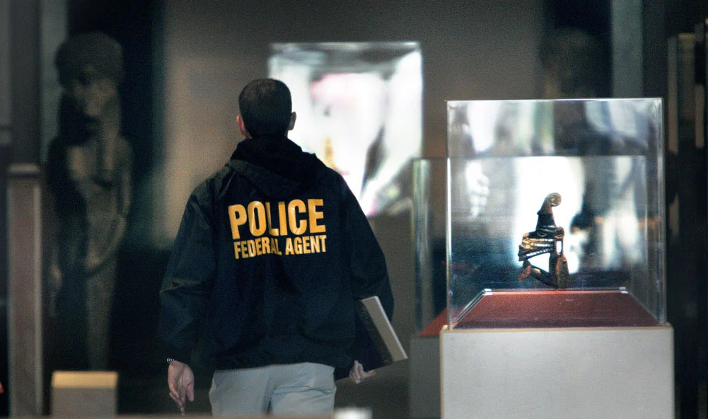 An FBI agent walks past a glass box containing a small statue from Ban Chiang