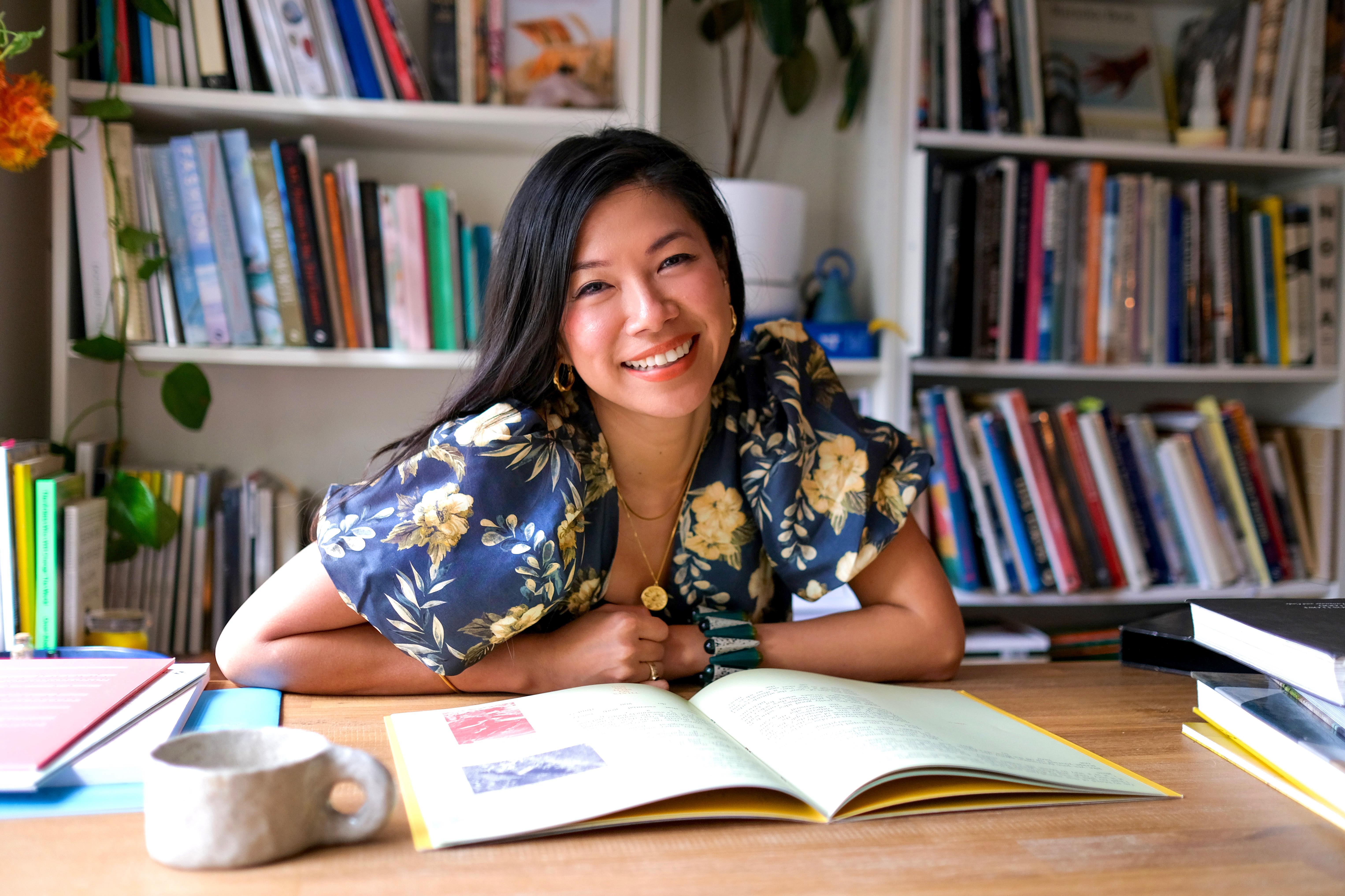 A photograph of a woman seated at a desk, smiling at the camera