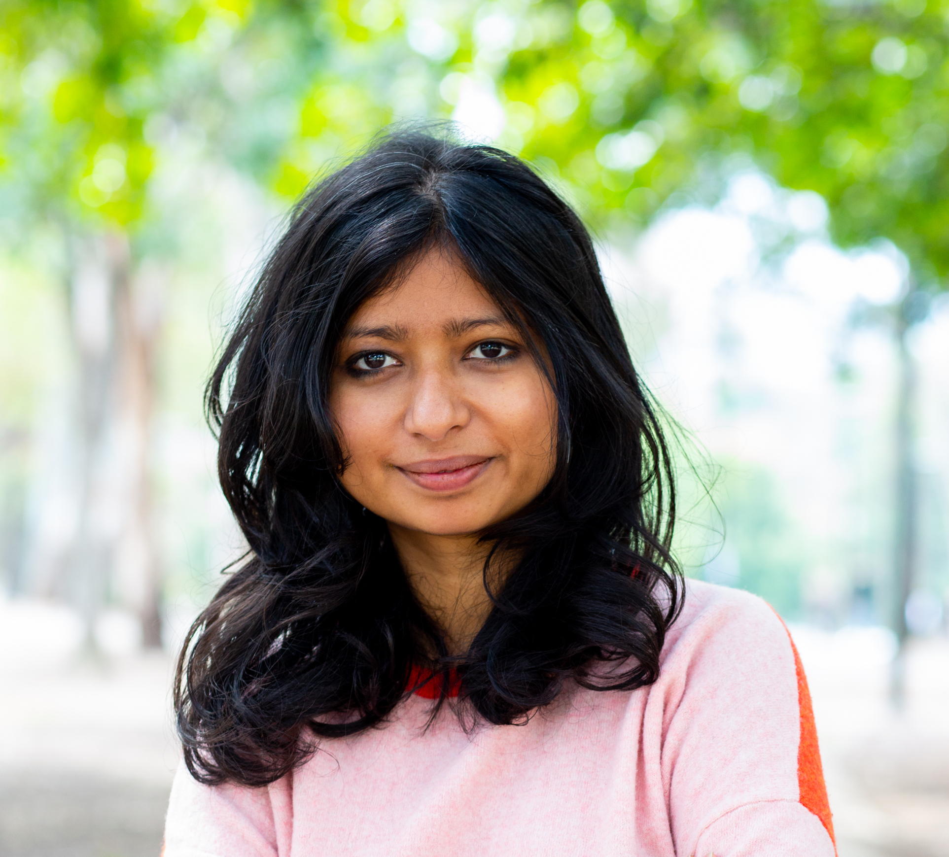 A woman with black hair and a pink top looks at the camera