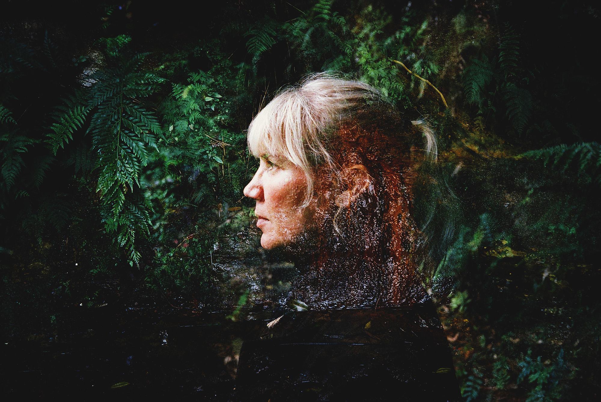 A photograph showing a woman in profile, against a backdrop of greenery.