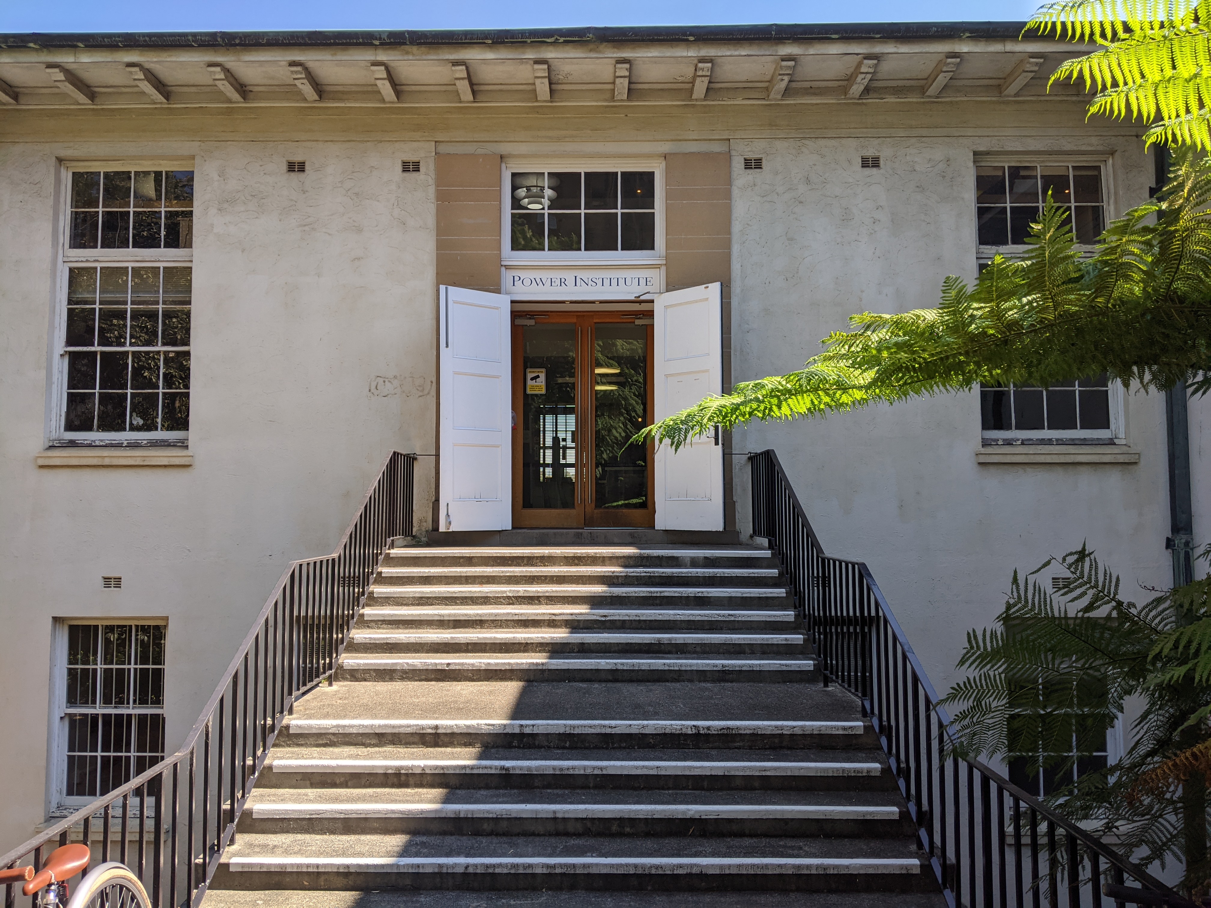 A photograph of a set of steps leading up to the entrance to the RC Mills building at the University of Sydney, above which hands a sign reading "Power Institute"