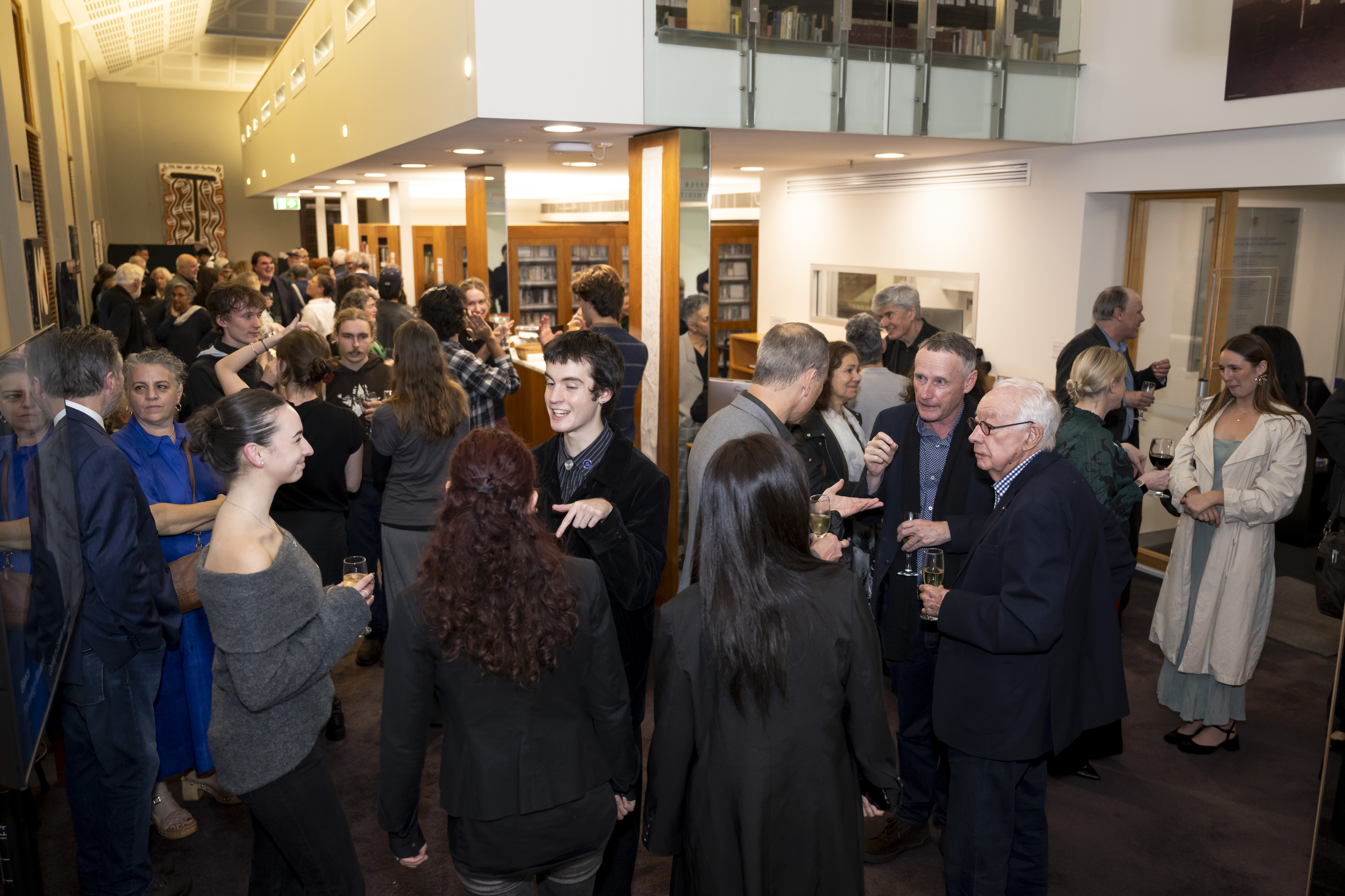 A photograph of a crowd of people standing and talking in the Schaeffer Library.