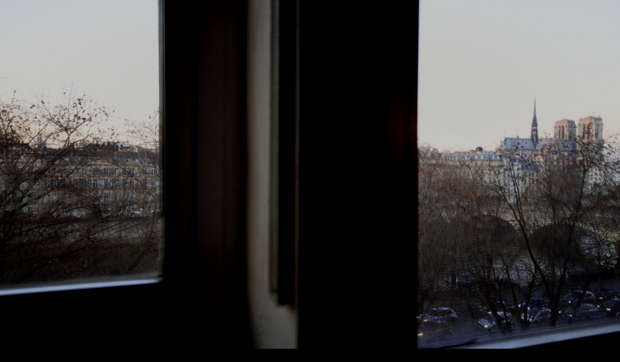 A still from a film that shows a view out a window of Paris, showing the Notre Dame in the distance.